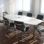 An empty white conference table sits in a room during late afternoon