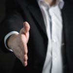 a man in a business suit extends his arm for a handshake at the beginning of a business relationship