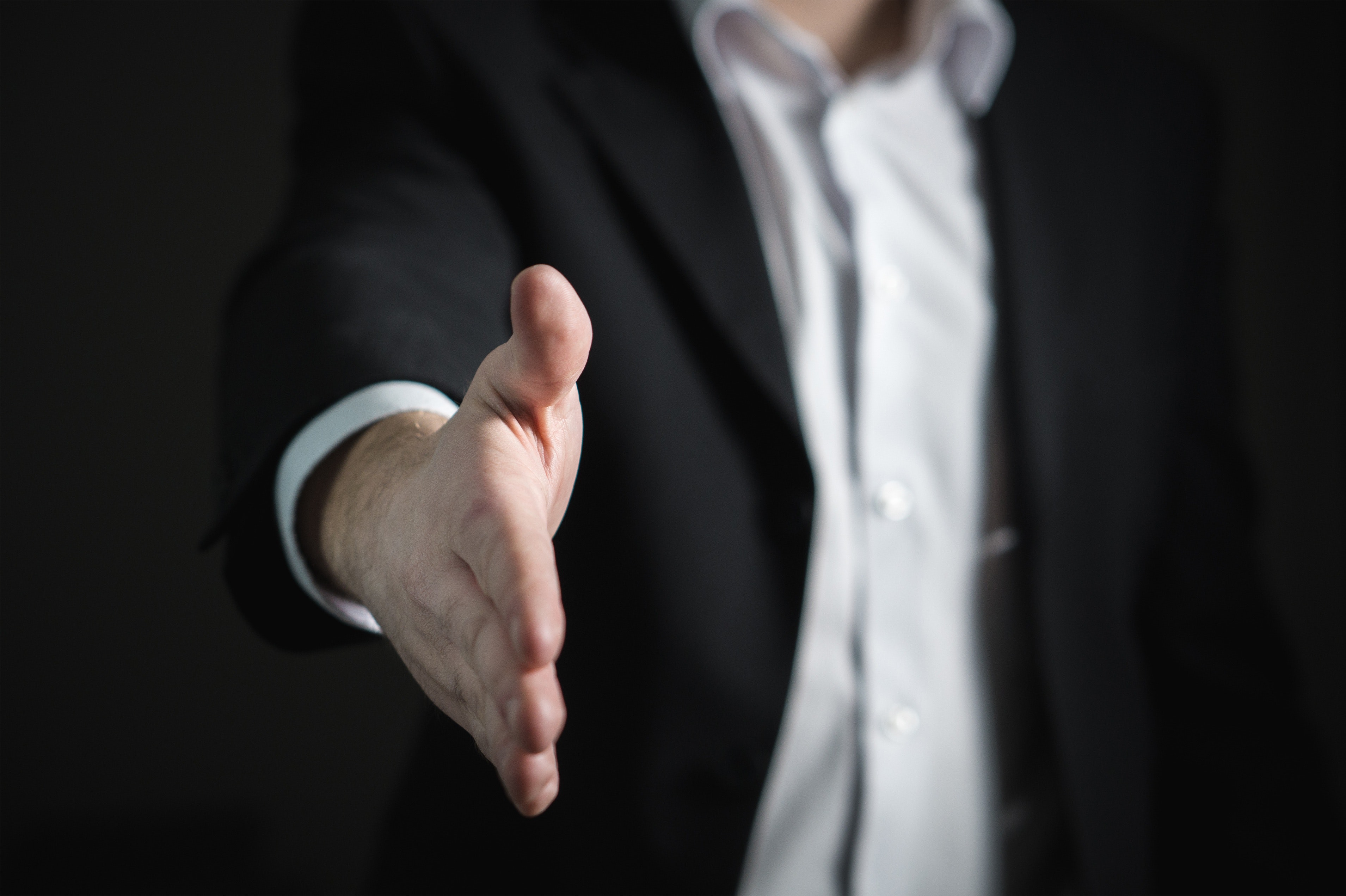 a man in a business suit extends his arm for a handshake at the beginning of a business relationship